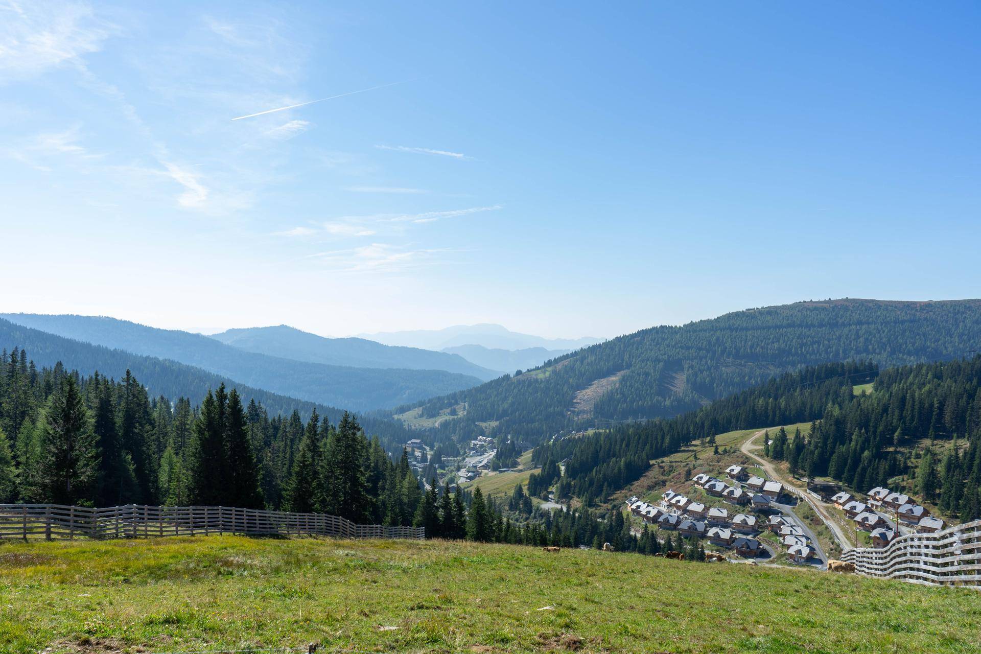 Weitläufiger Panoramablick über ein Bergtal mit einem kleinen Dorf und bewaldeten Hängen.