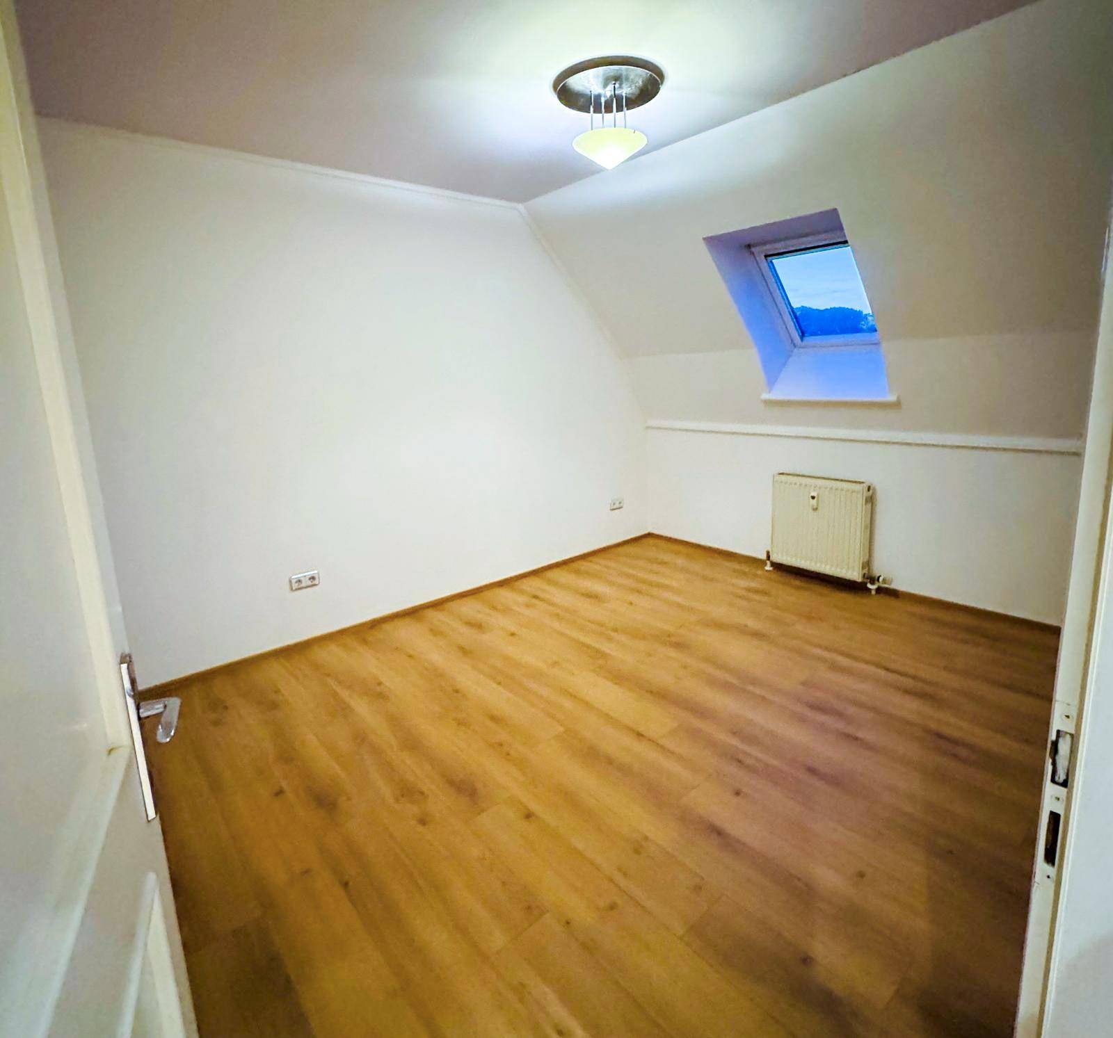 Leeres Zimmer mit Dachschräge, Holzboden und Dachfenster.