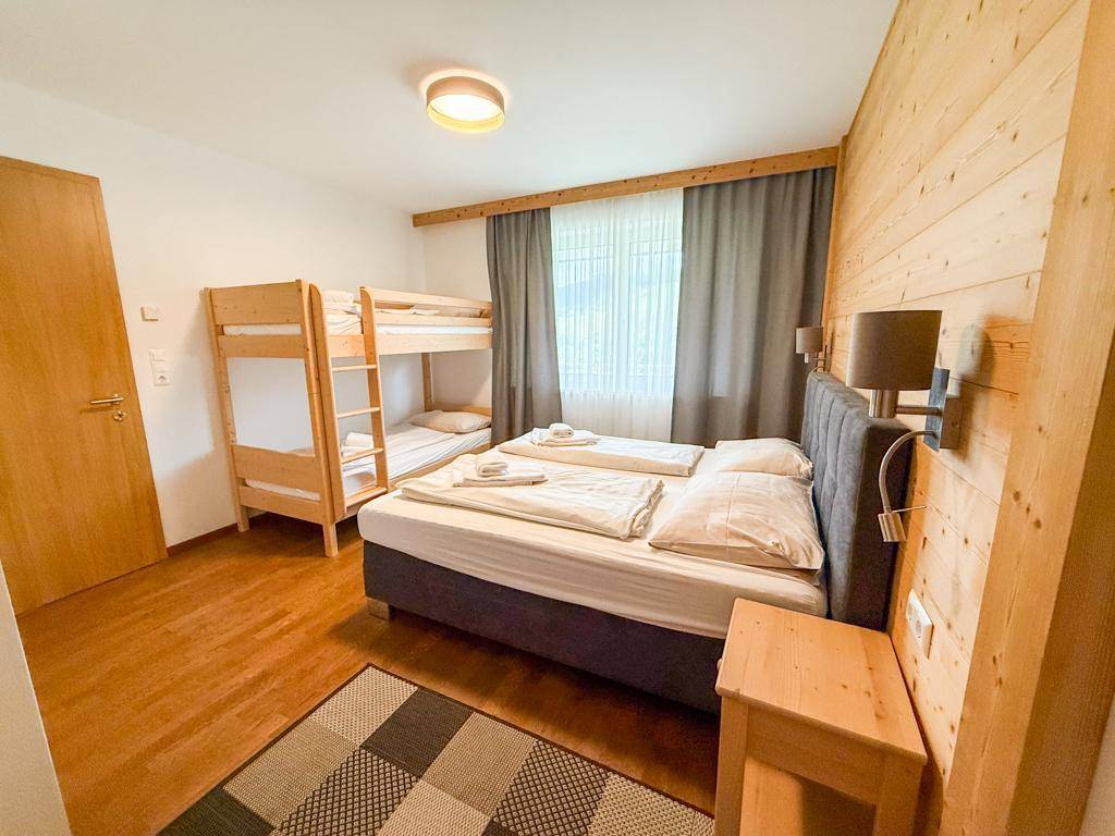 Gemütliches Schlafzimmer mit Doppelbett, Etagenbett und Holzwandverkleidung.