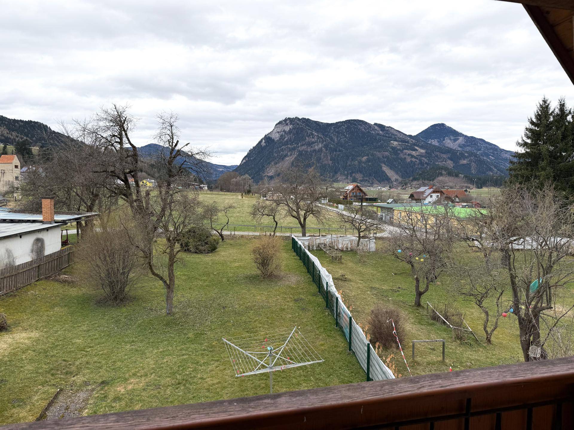 Blick vom Balkon auf den weitläufigen Gartenbereich und die umliegende Berglandschaft.