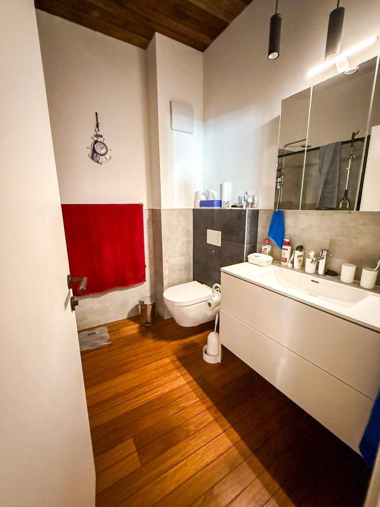 Badezimmer mit modernem Waschbecken, Spiegelschrank, Wand-WC und Holzfußboden.
