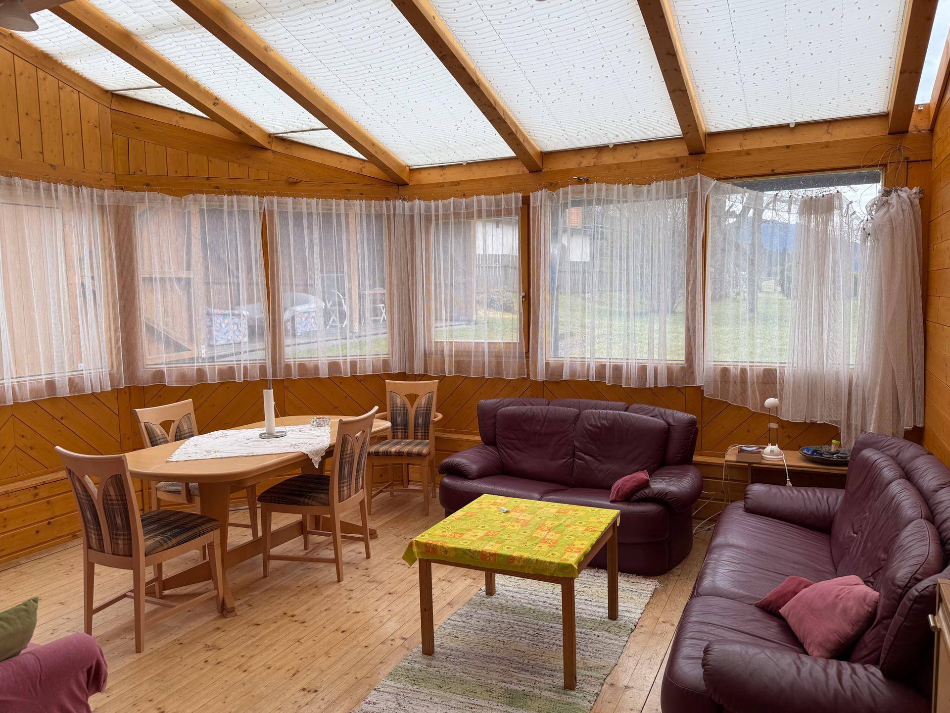 Heller Wintergarten mit Holzverkleidung, Esstisch und bequemen Ledersofas.