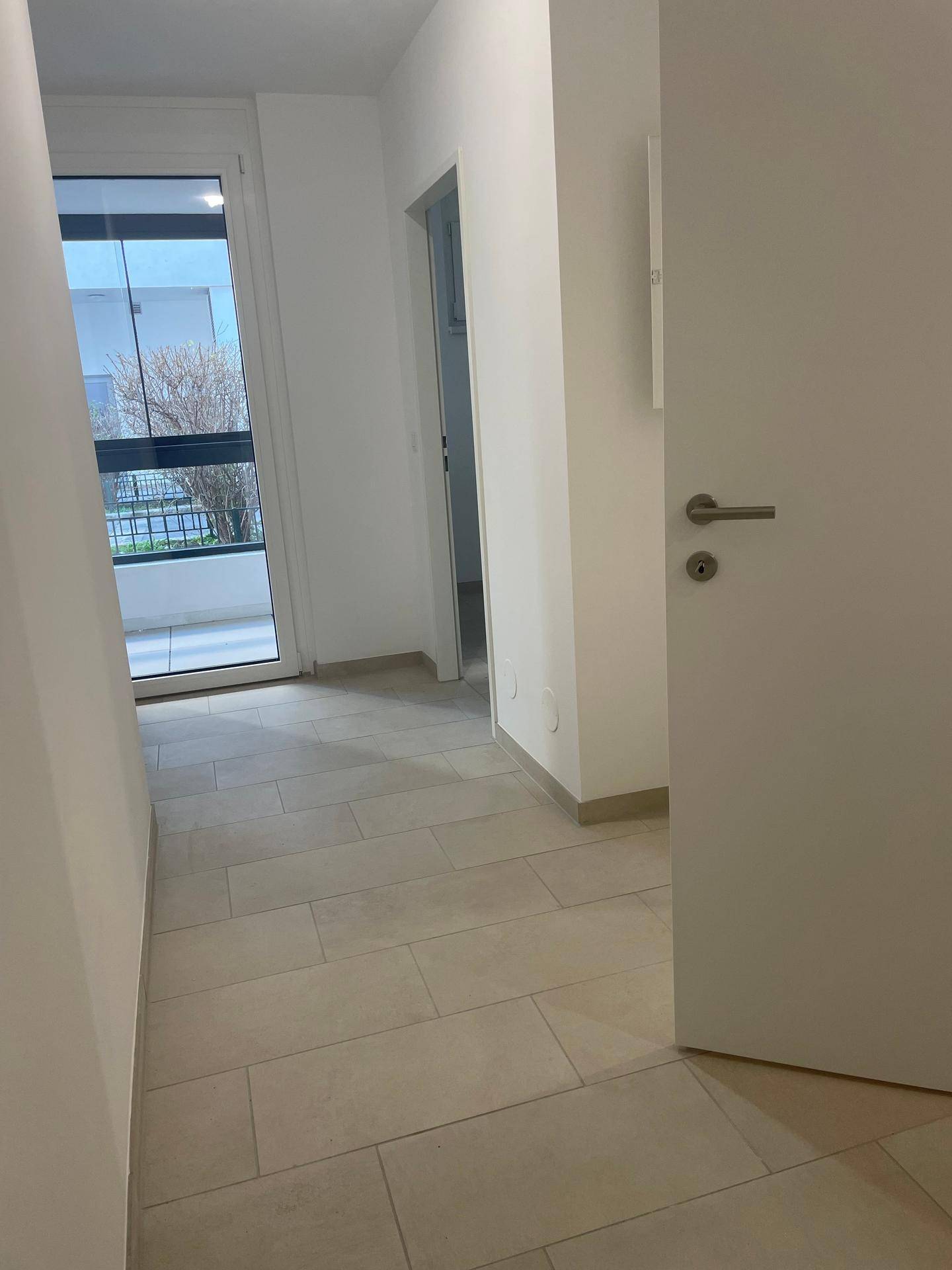 Heller Flur mit Fliesenboden und Zugang zu einem Balkon oder einer Loggia.