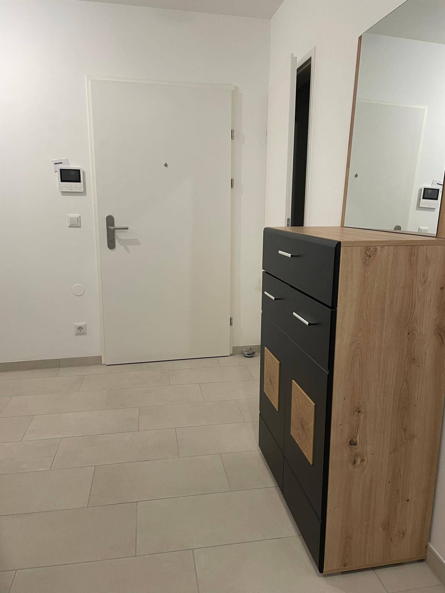 Eingangsbereich mit Fliesenboden, moderner Kommode und Spiegel, sowie der Wohnungstür.