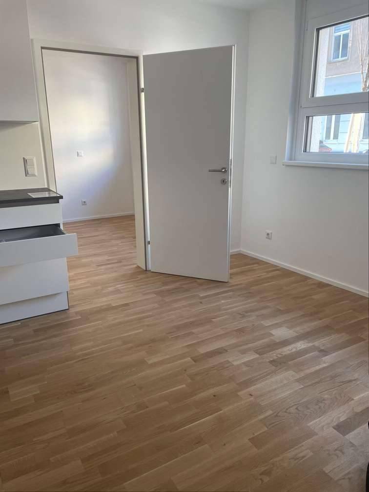 Heller Raum mit Holzboden und weiß gestrichenen Wänden, Blick durch eine offene Tür.