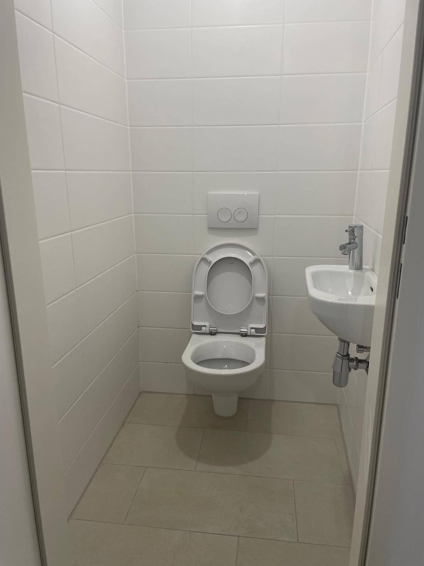 Kleines Gäste-WC mit wandhängender Toilette, kleinem Waschbecken und weißen Fliesen.