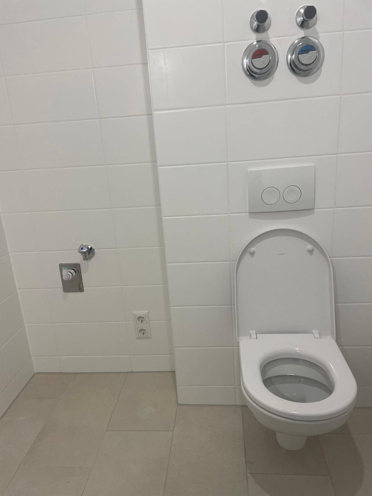 Separates WC mit wandhängender Toilette und Anschlüssen für eine Waschmaschine.