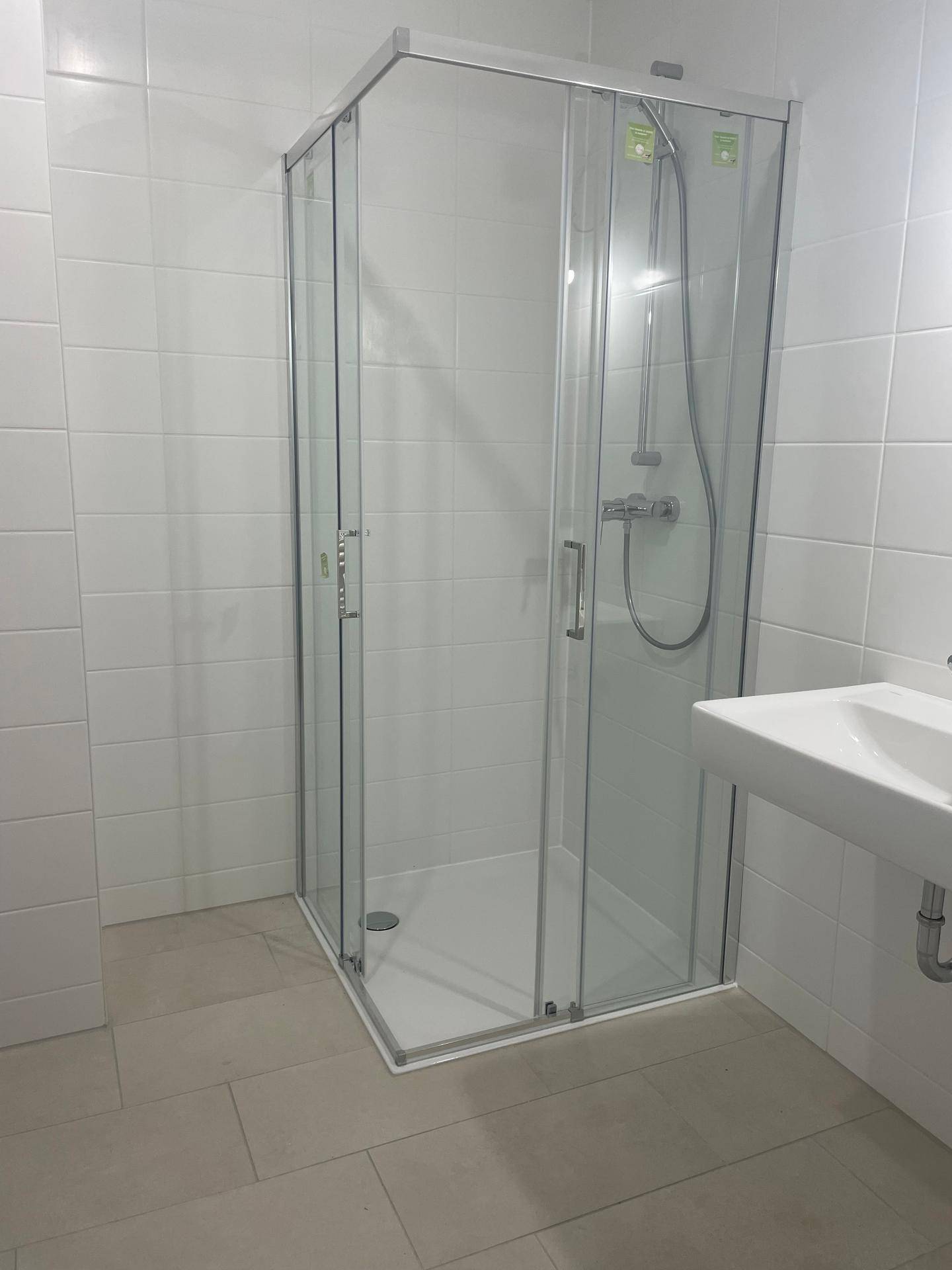 Modernes Badezimmer mit Duschkabine, weißen Wandfliesen und hellem Fliesenboden.