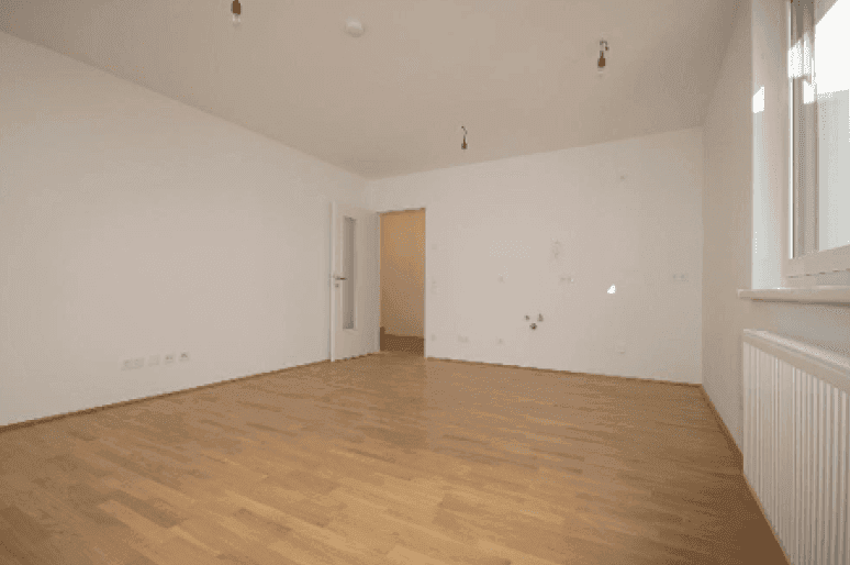 Geräumiges, unmöbliertes Zimmer mit hellem Parkettboden und Zugang zu weiteren Räumen.