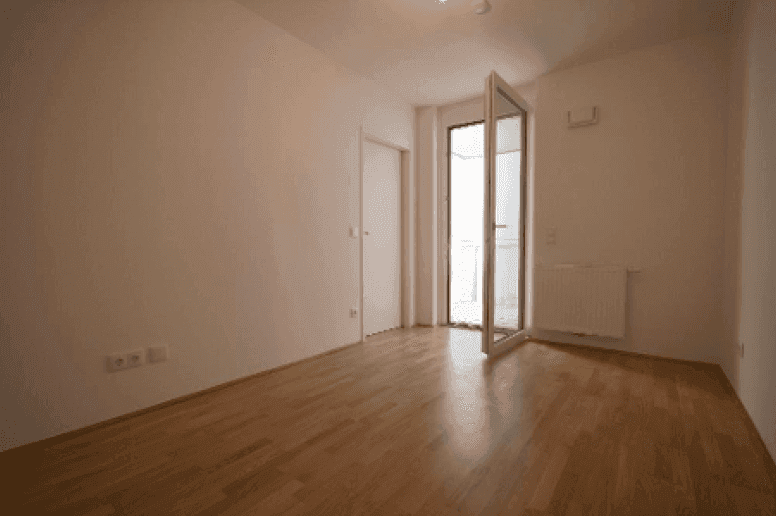 Helles Zimmer mit Parkettboden und offenem Zugang zu einem Balkon, bietet viel Tageslicht.