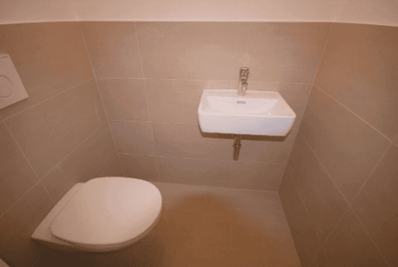 Kompaktes Gäste-WC mit beigefarbenen Fliesen, wandhängendem WC und kleinem Handwaschbecken.