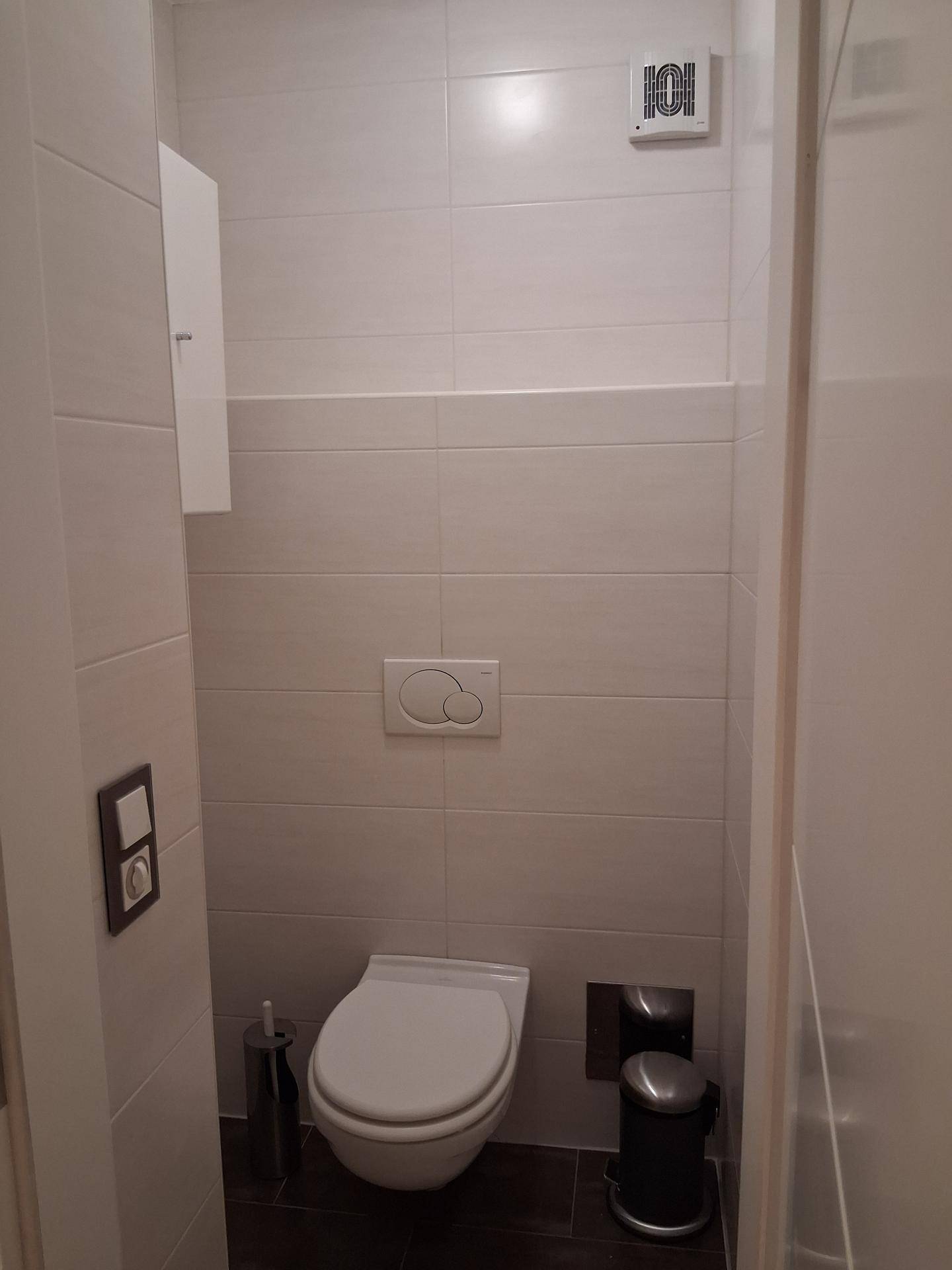 Kleines Gäste-WC mit Wand-WC, Fliesen an Wänden und Boden sowie einem Abluftventilator.