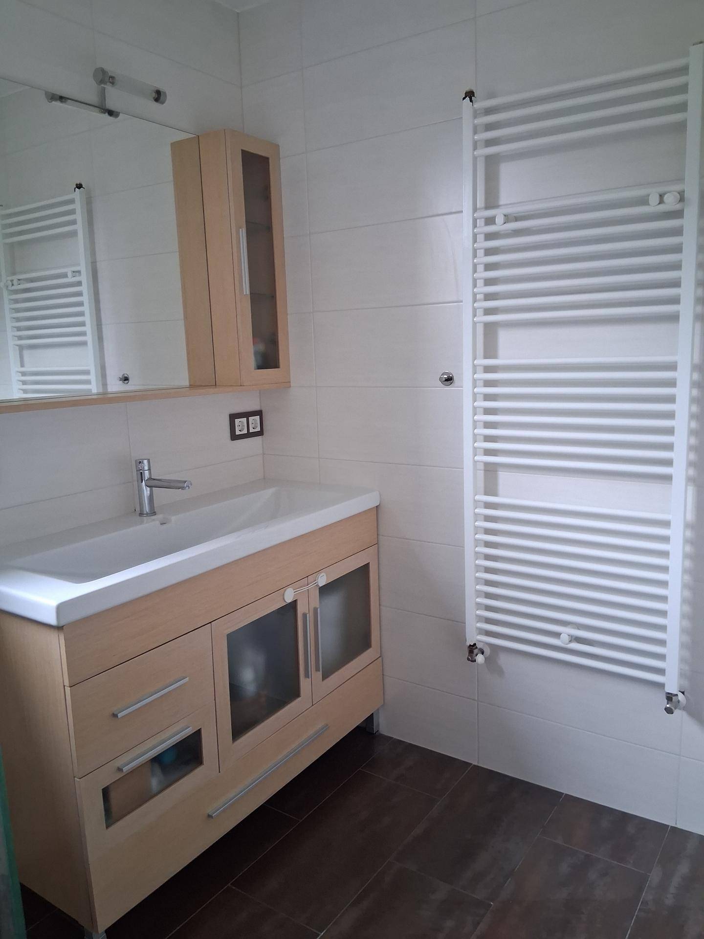 Badezimmer mit modernem Waschtisch, Spiegelschrank und beheiztem Handtuchhalter an der Wand.