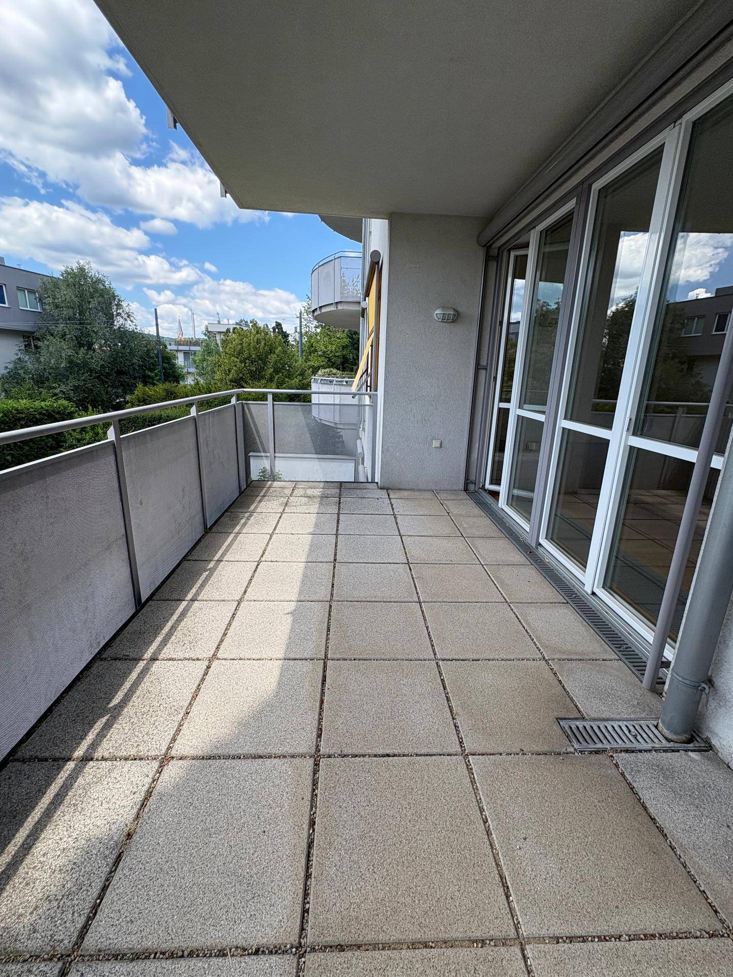 Geräumiger Balkon mit Fliesenboden und Blick auf die Umgebung und Bäume.