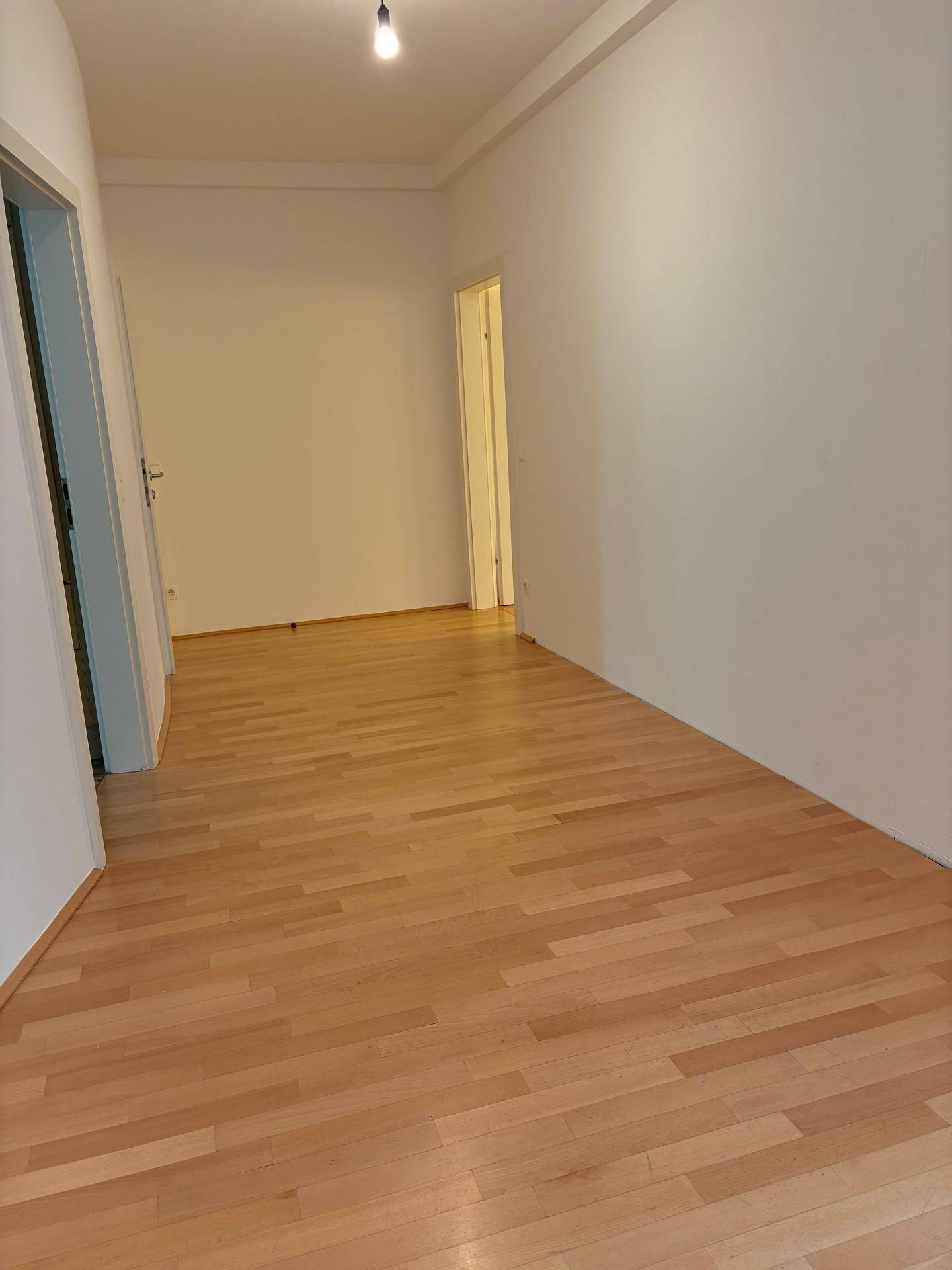Leerer Raum mit hellem Holzparkett und weißen Wänden, bereit zur individuellen Gestaltung.