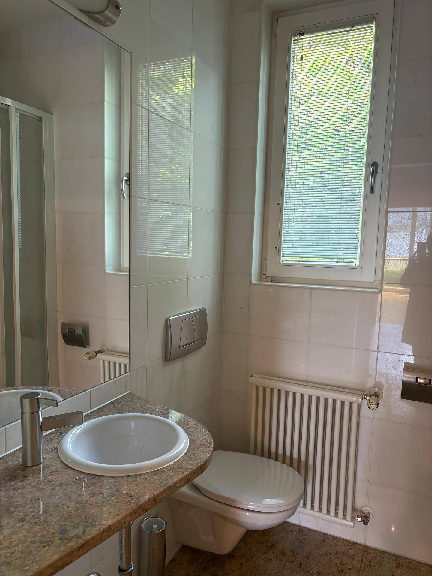 Kleines Badezimmer mit WC, Waschtisch, Fenster und einem Heizkörper.