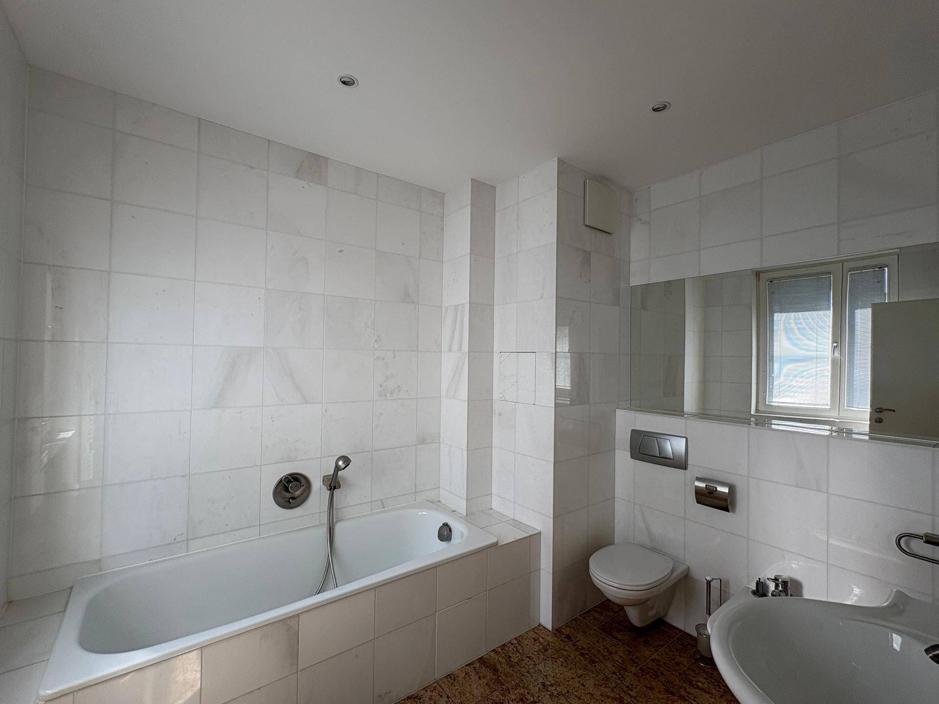 Badezimmer mit weiß gefliesten Wänden, Badewanne, WC und einem Waschtischbereich.