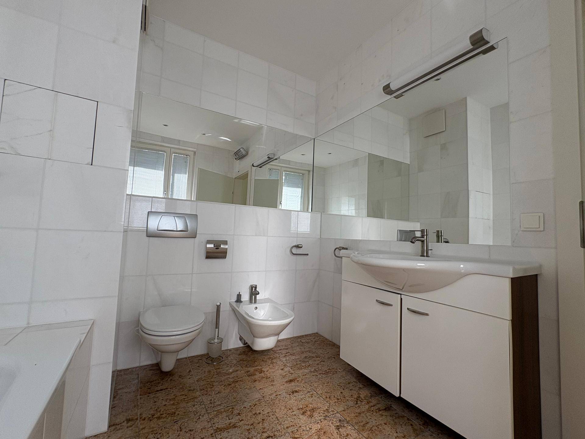 Modernes Badezimmer mit weißen Fliesen, WC, Bidet und einem Waschtisch mit großem Spiegel.