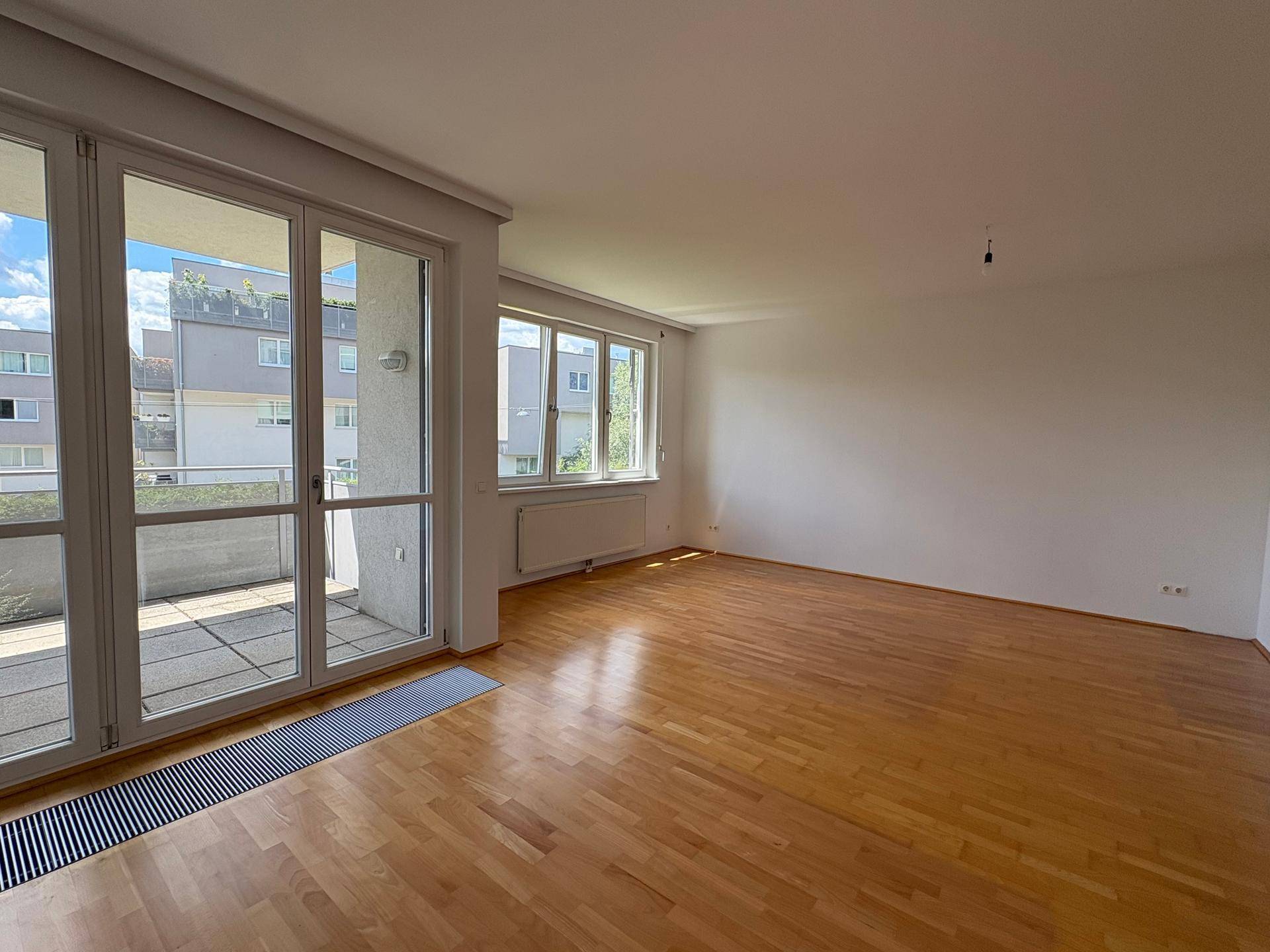 Heller Wohnbereich mit Holzparkett und breiter Fensterfront, die auf eine Terrasse führt.