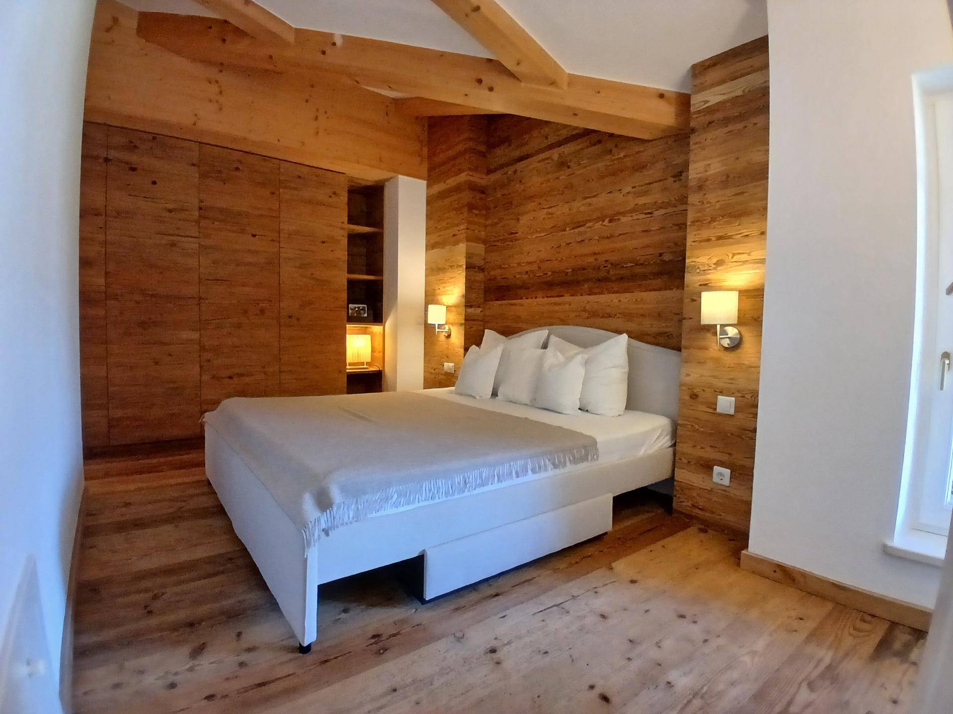 Gemütliches Schlafzimmer mit Holzwänden, Holzbalken und großem Doppelbett.