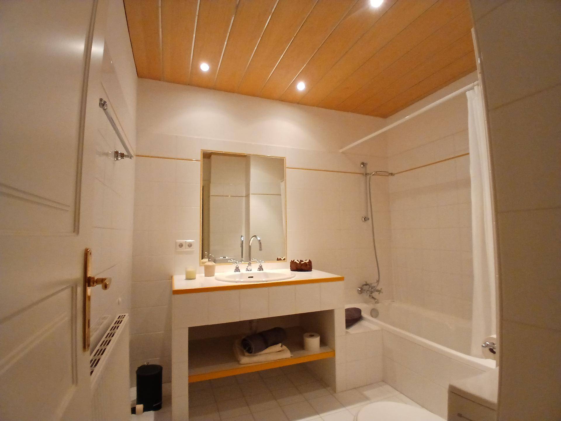 Helles Badezimmer mit Badewanne, Waschbecken und Holzdecke.