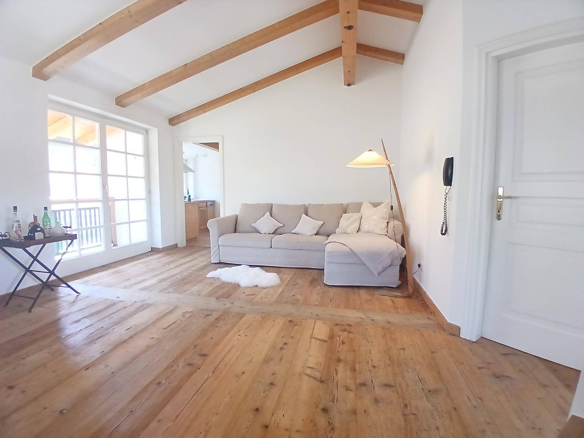 Heller Wohnbereich mit Holzboden, bequemer Couch und Zugang zu einem Balkon.