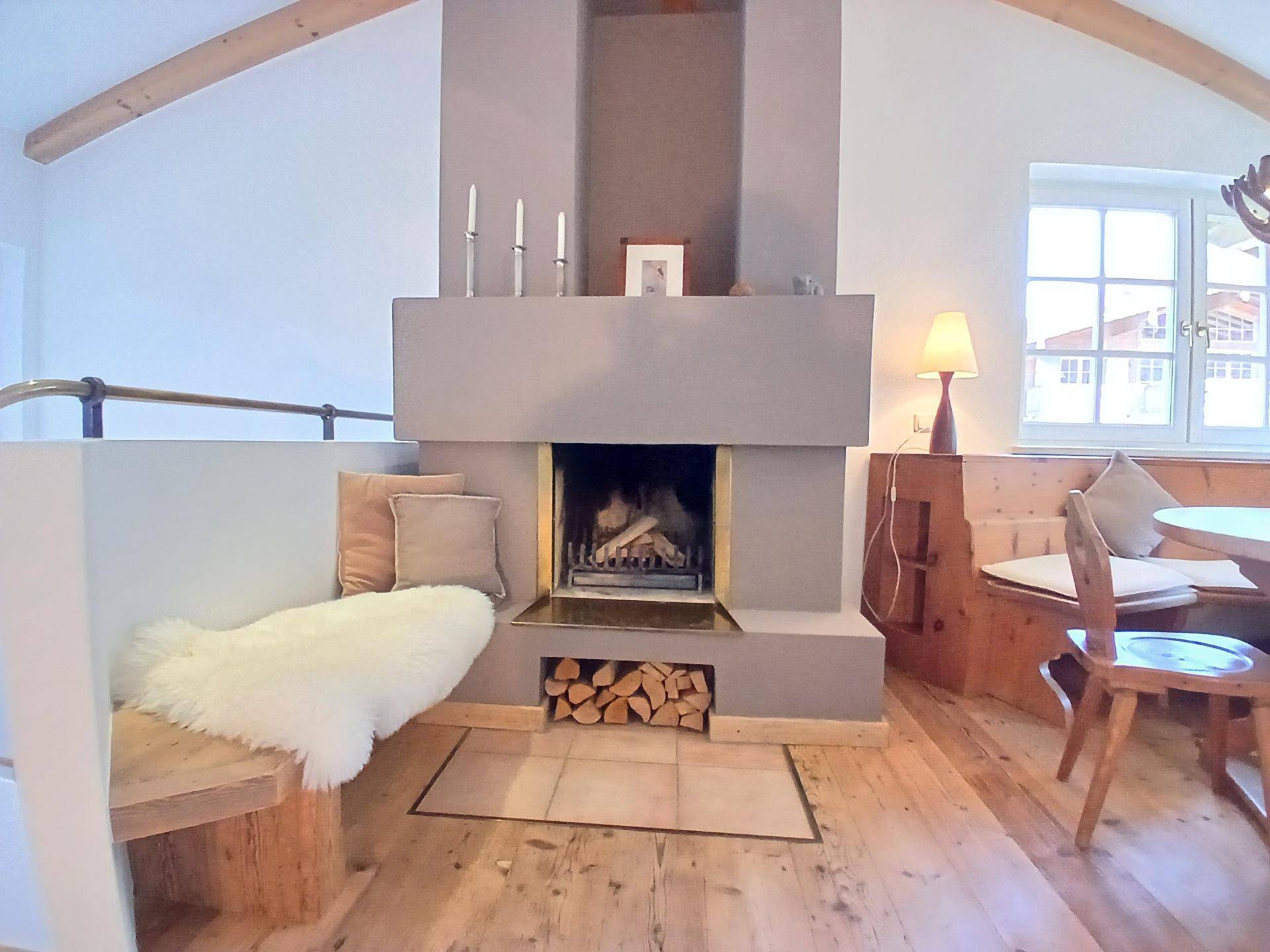Detailansicht des Kamins mit Holzscheiten und einer gemütlichen Sitzbank im Wohnbereich.