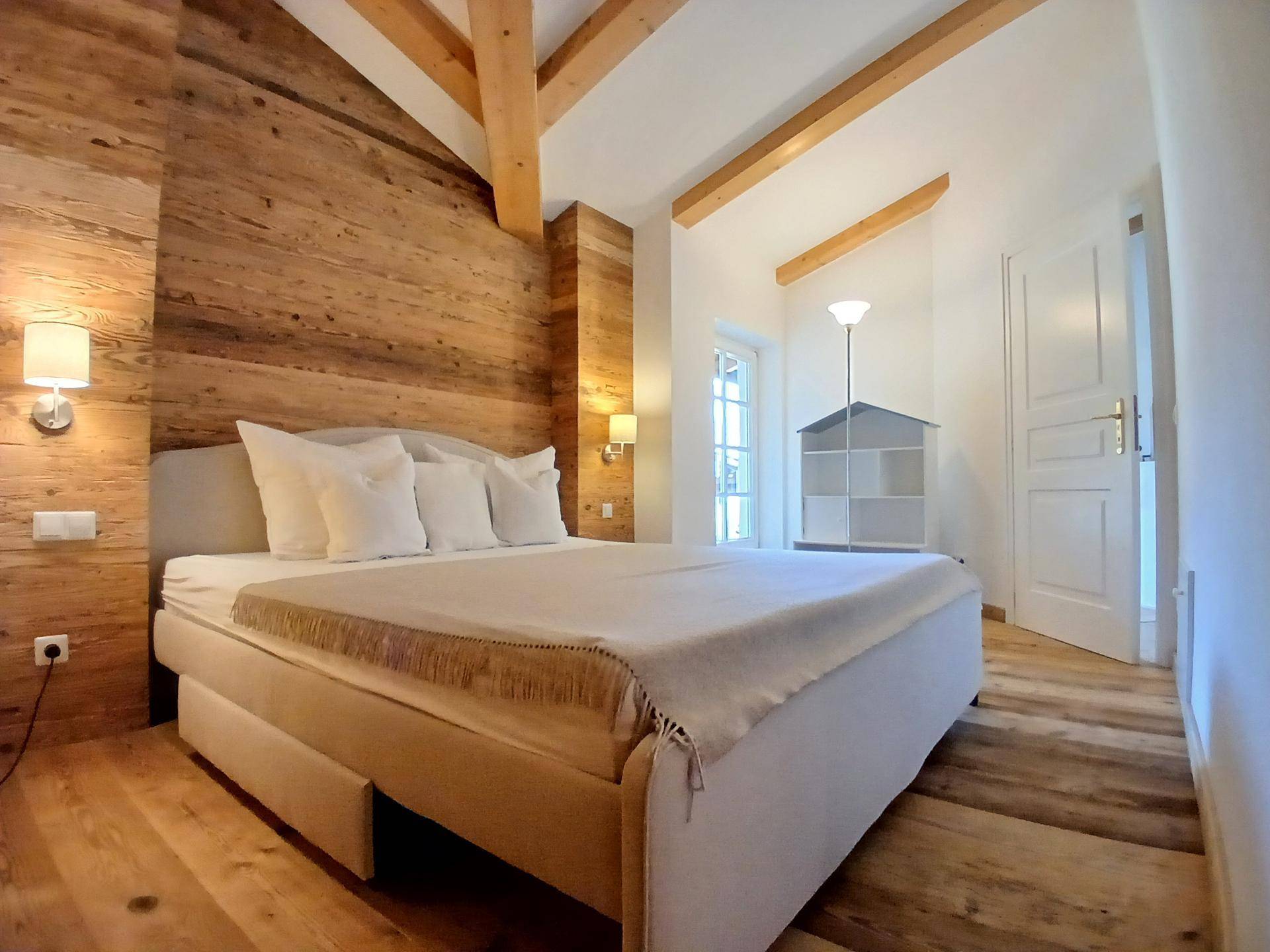 Helles Schlafzimmer mit Holzwänden, Holzbalken und Blick nach draußen.