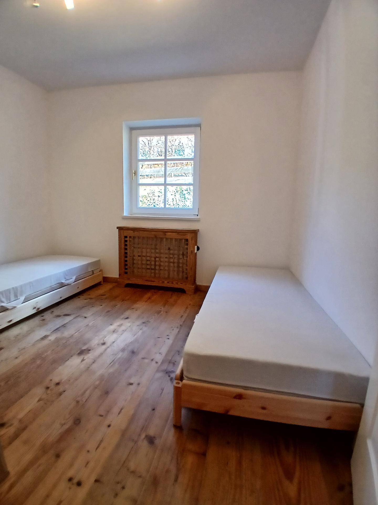 Einfaches Schlafzimmer mit zwei Einzelbetten, Holzboden und Fenster.