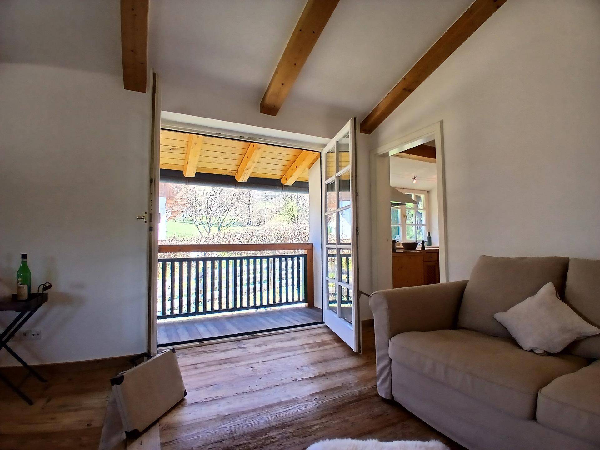 Wohnbereich mit Holzboden und direktem Zugang zu einem überdachten Balkon.