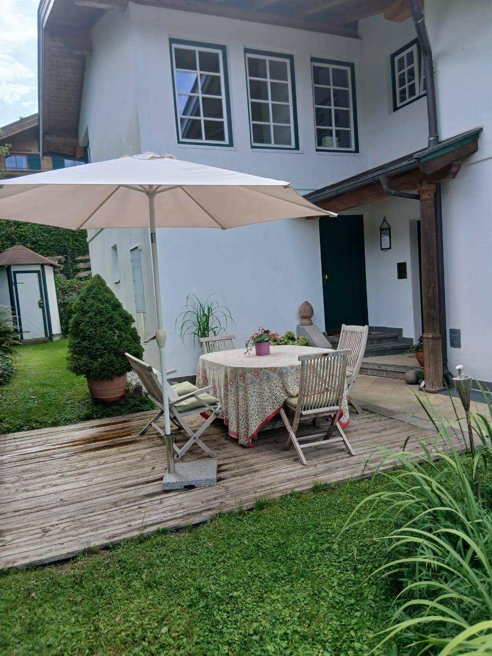 Gemütliche Holzterrasse mit Sonnenschirm und Sitzgelegenheiten neben dem Haus.