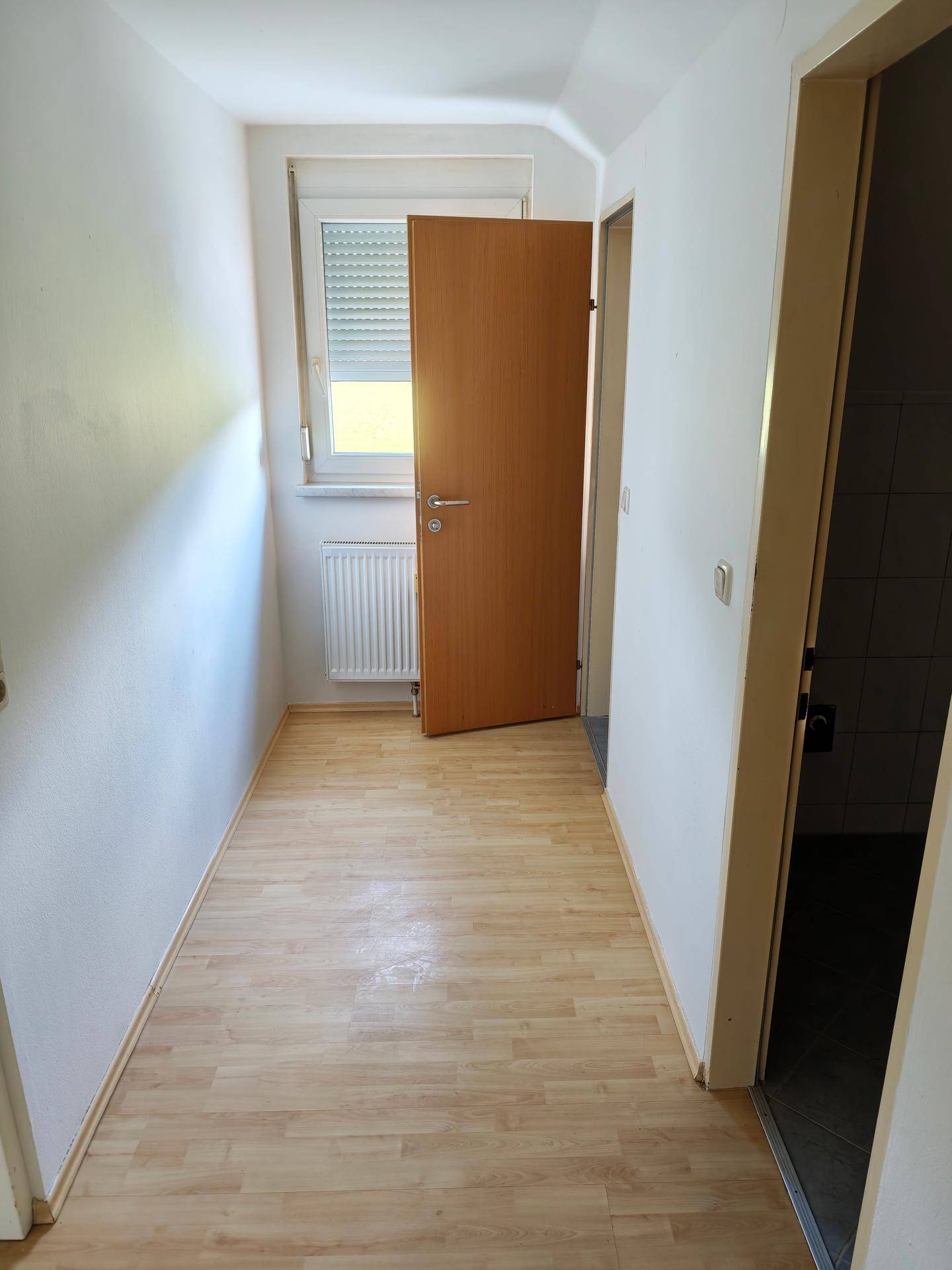 Heller Flur mit Laminatboden, Fenster und Heizkörper, der zu weiteren Räumen führt.