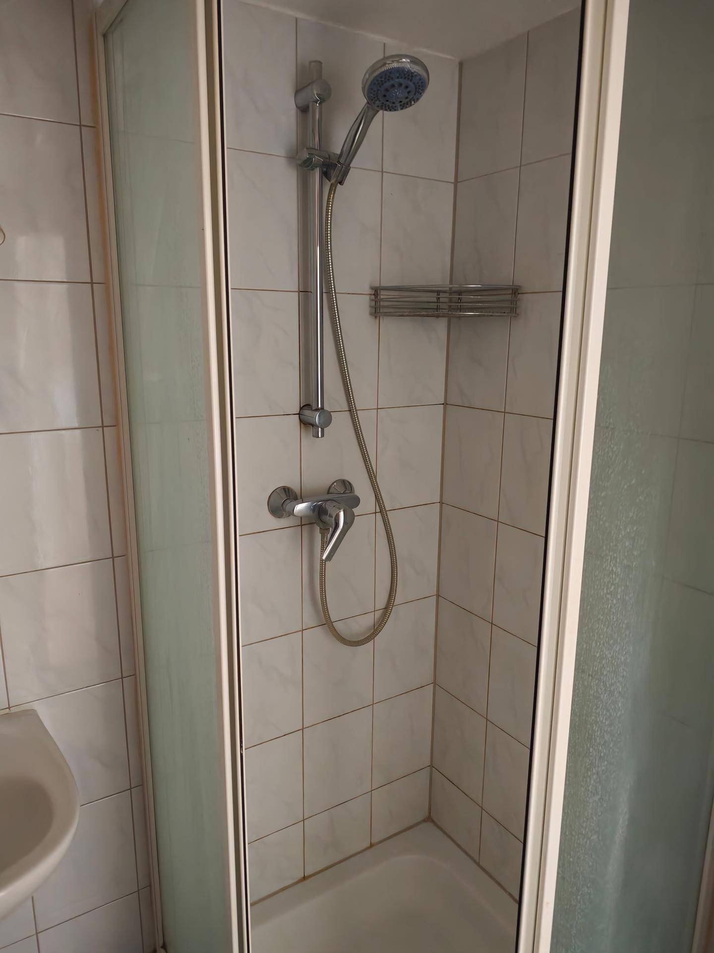 Duschkabine mit weißen Fliesen und einfacher Duscharmatur in einem funktionalen Badezimmer.