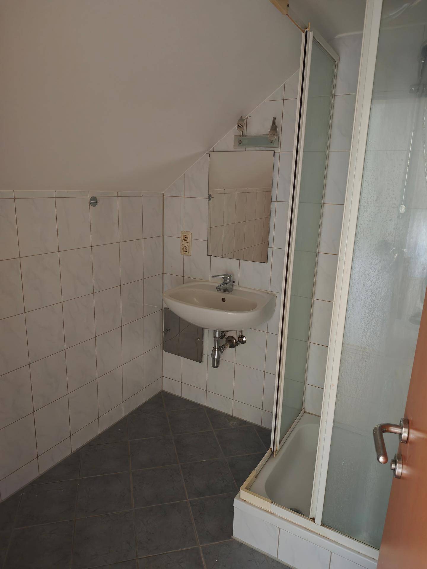 Badezimmer mit Dachschräge, Duschkabine, Waschbecken und Spiegel in schlichtem Design.