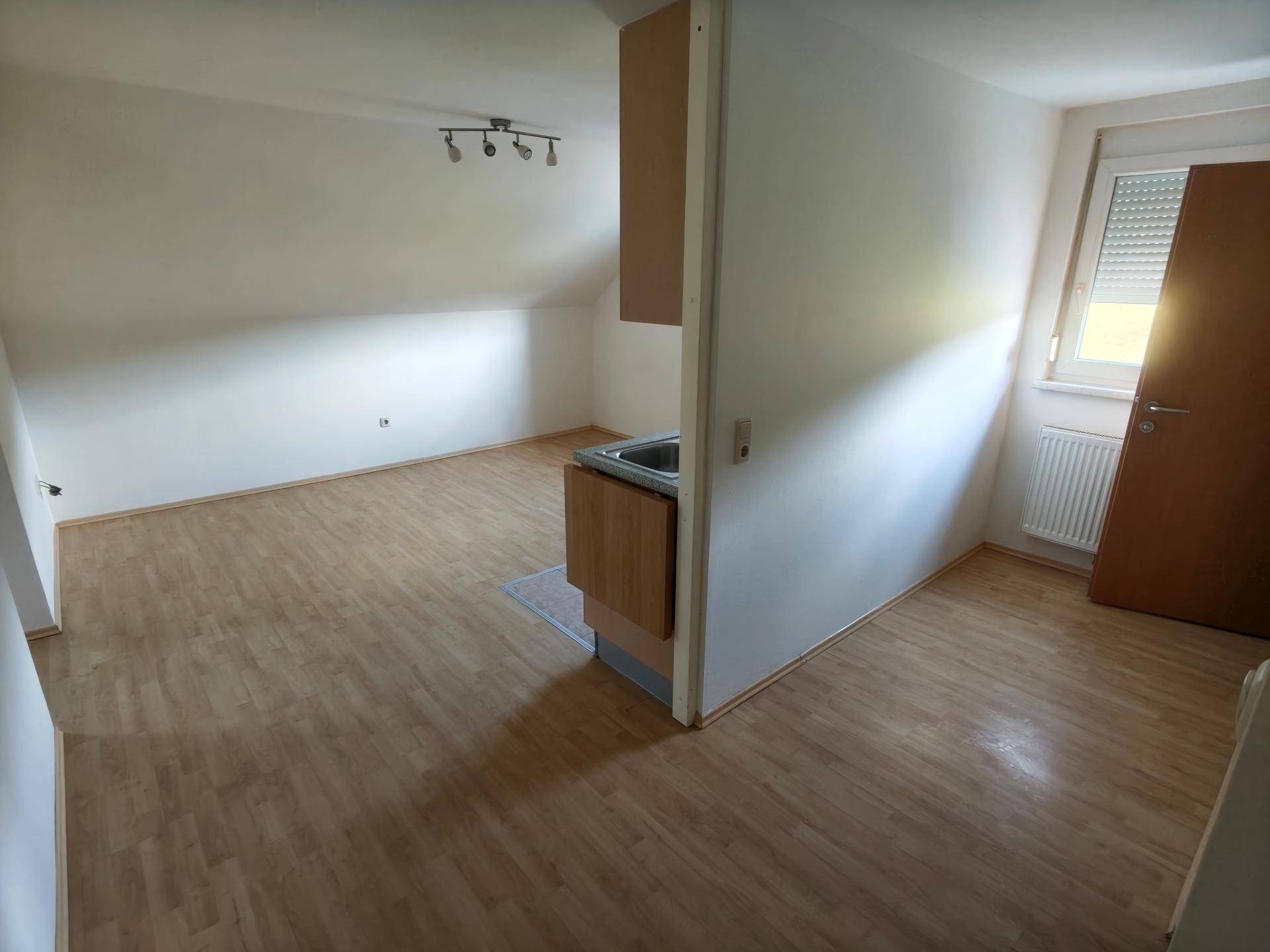 Offener Wohnbereich mit integrierter Küchenzeile, Laminatboden und Dachschräge.