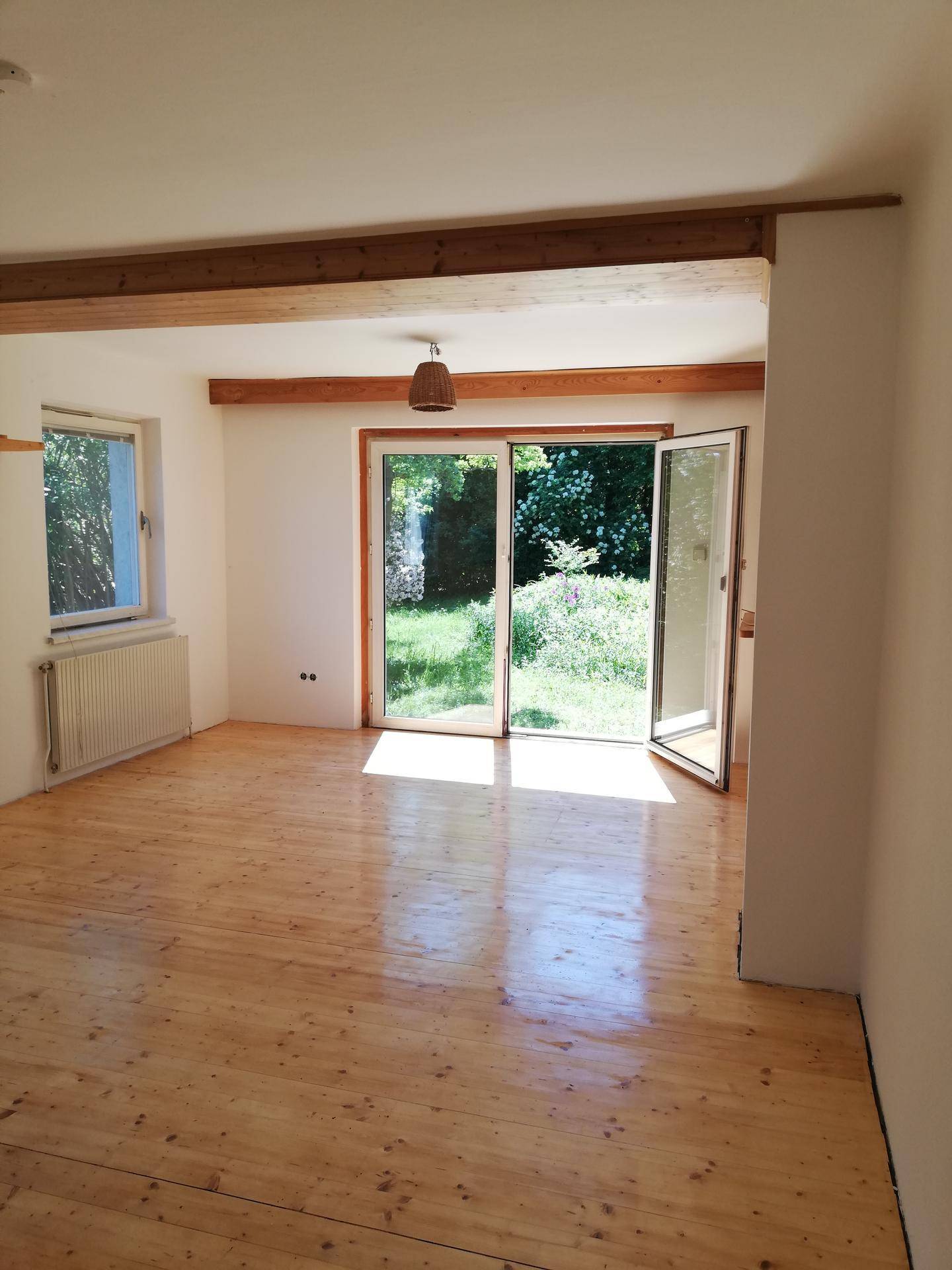 Heller Wohnraum mit Holzboden, sichtbaren Holzbalken und großem Zugang zum Garten.