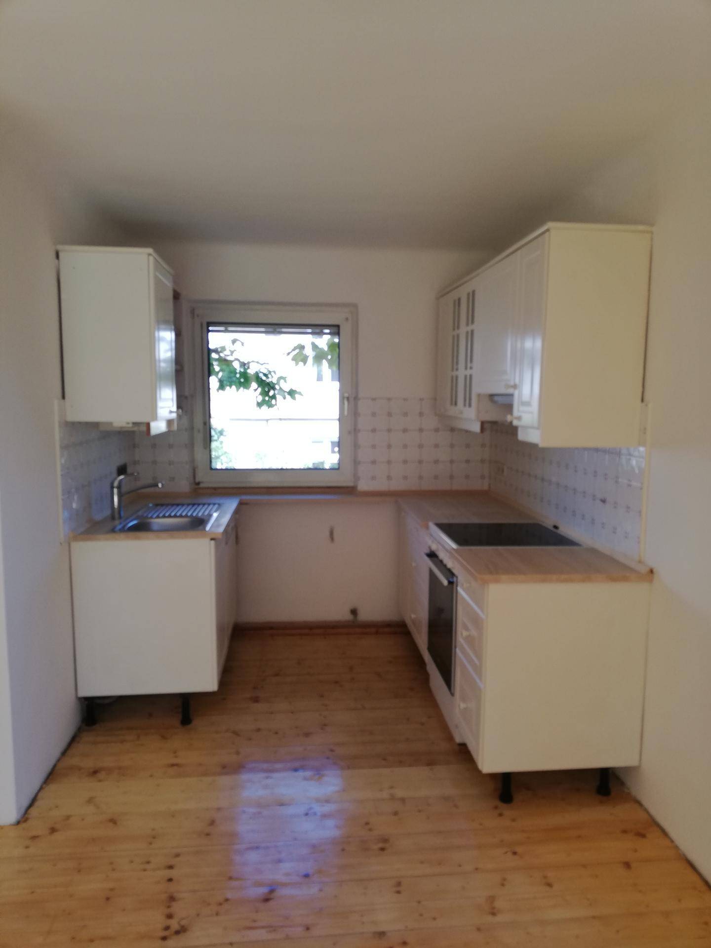 Kleine Küche mit weißen Schränken, Holzarbeitsplatten und Fenster über der Spüle.