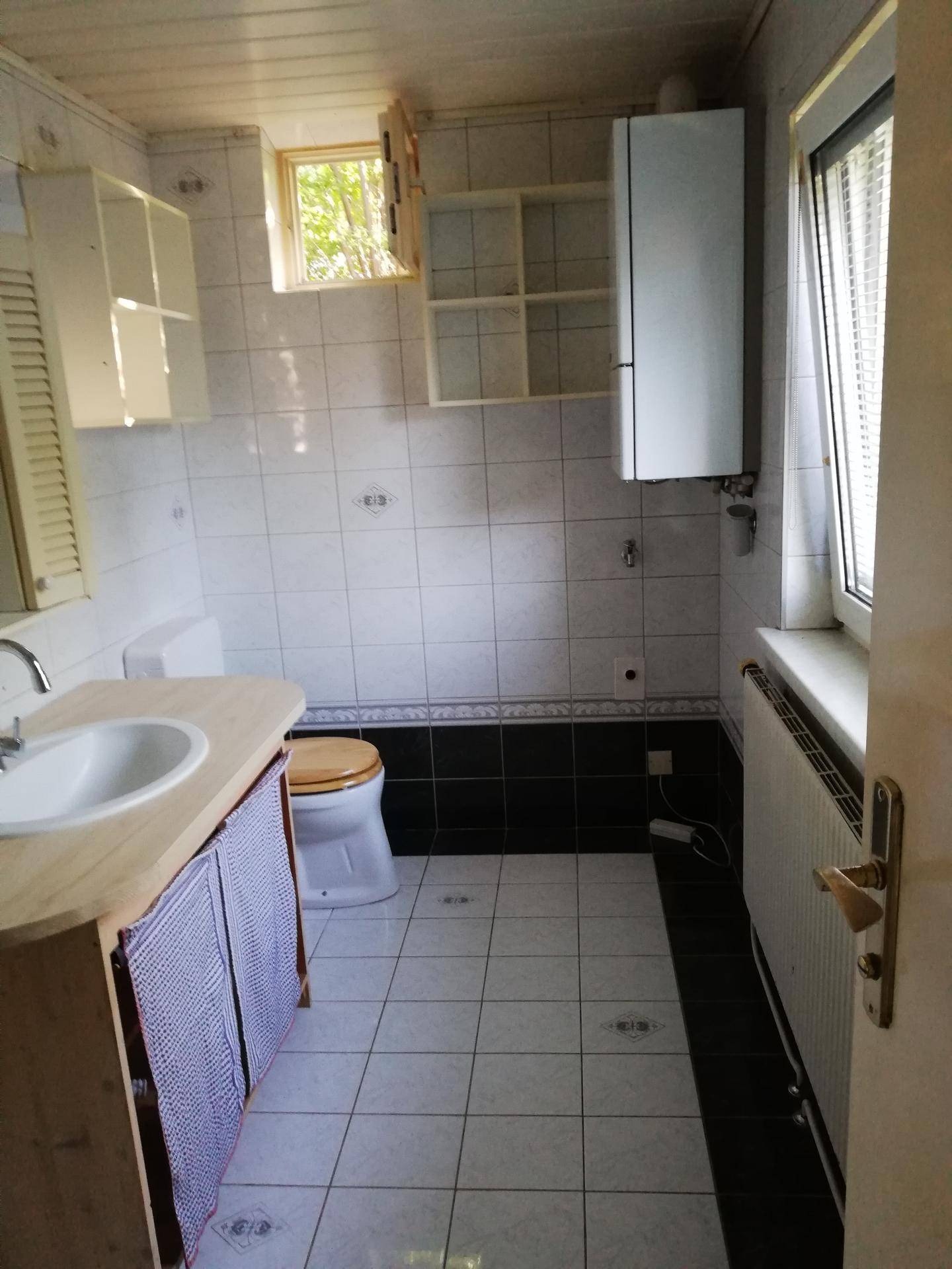 Badezimmer mit weißen und schwarzen Fliesen, WC, Waschtisch und Fenster.