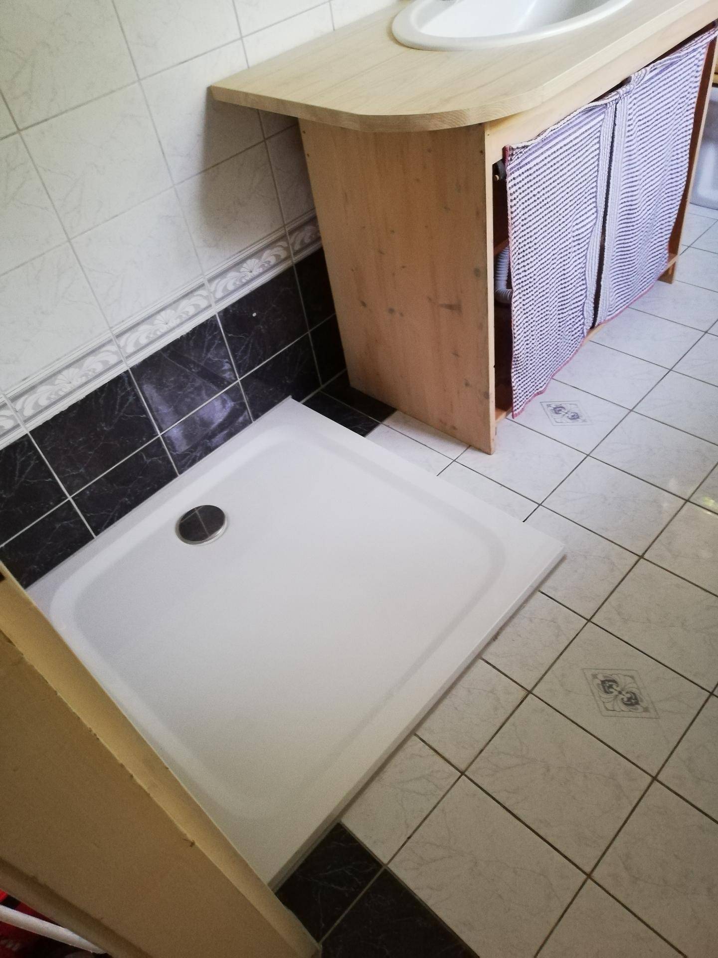 Detailansicht des Badezimmers mit Duschwanne und Waschtisch mit Holzunterschrank.