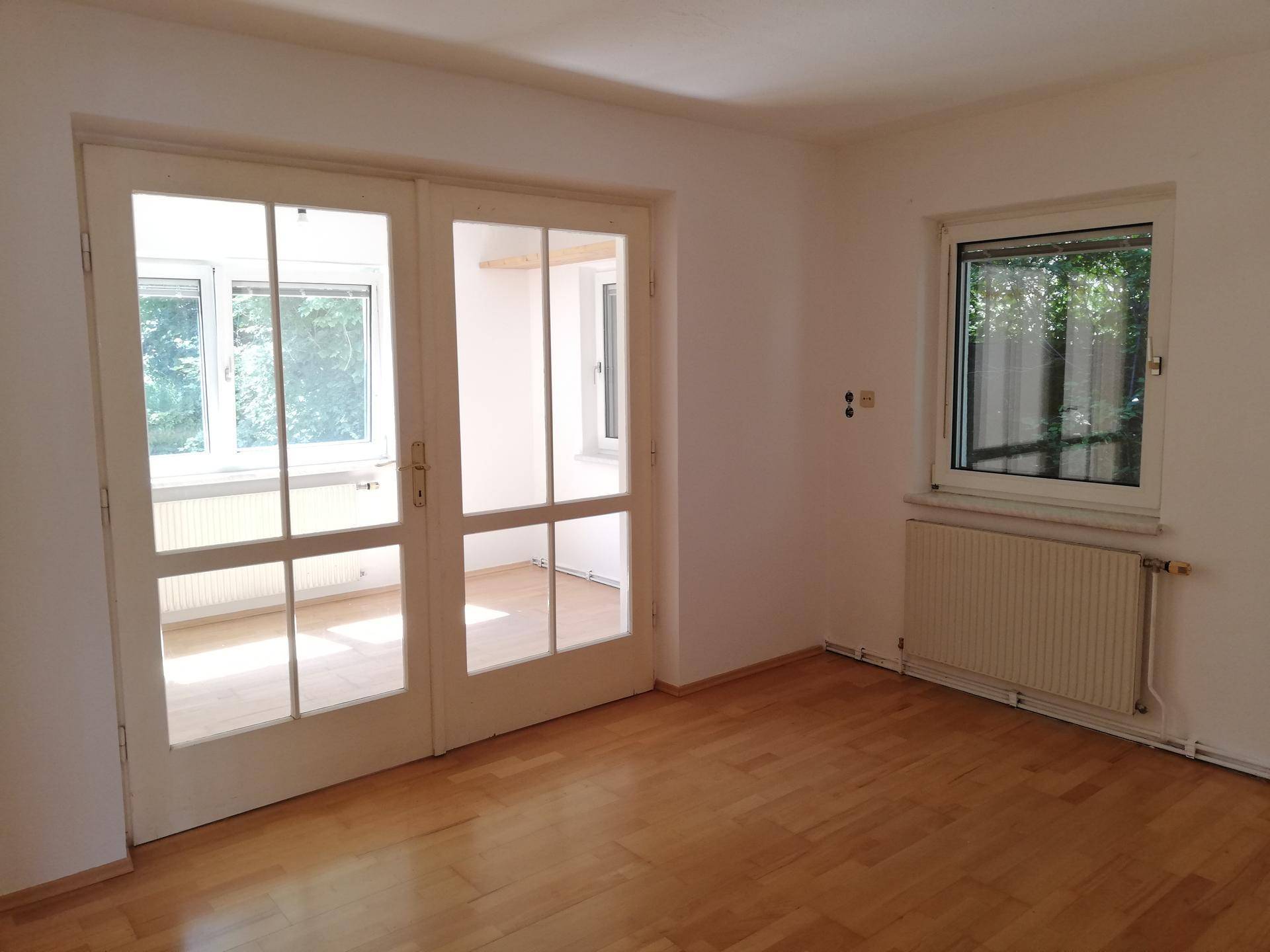 Wohnraum mit Holzboden, Heizkörper unter dem Fenster und Doppeltüren.