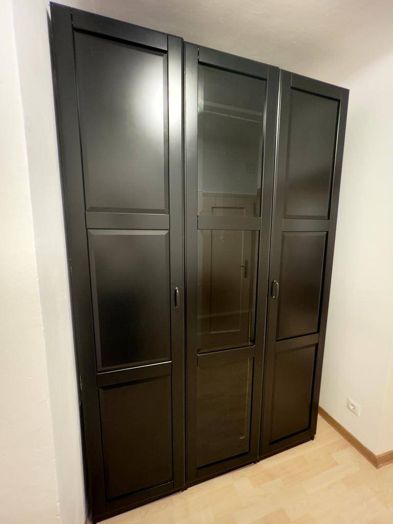 Großer, dunkler Kleiderschrank mit drei Türen und integrierten Glaspaneelen für Stauraum.