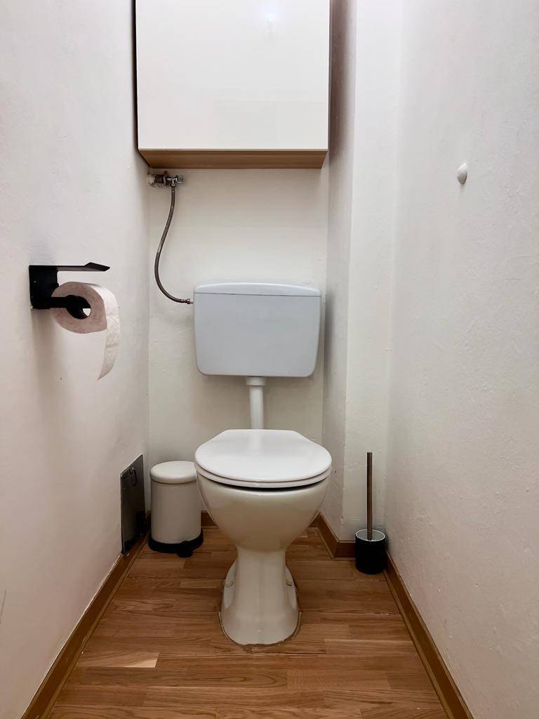 Separates WC mit Toilette und kleinem Mülleimer, einfach und funktional ausgestattet.