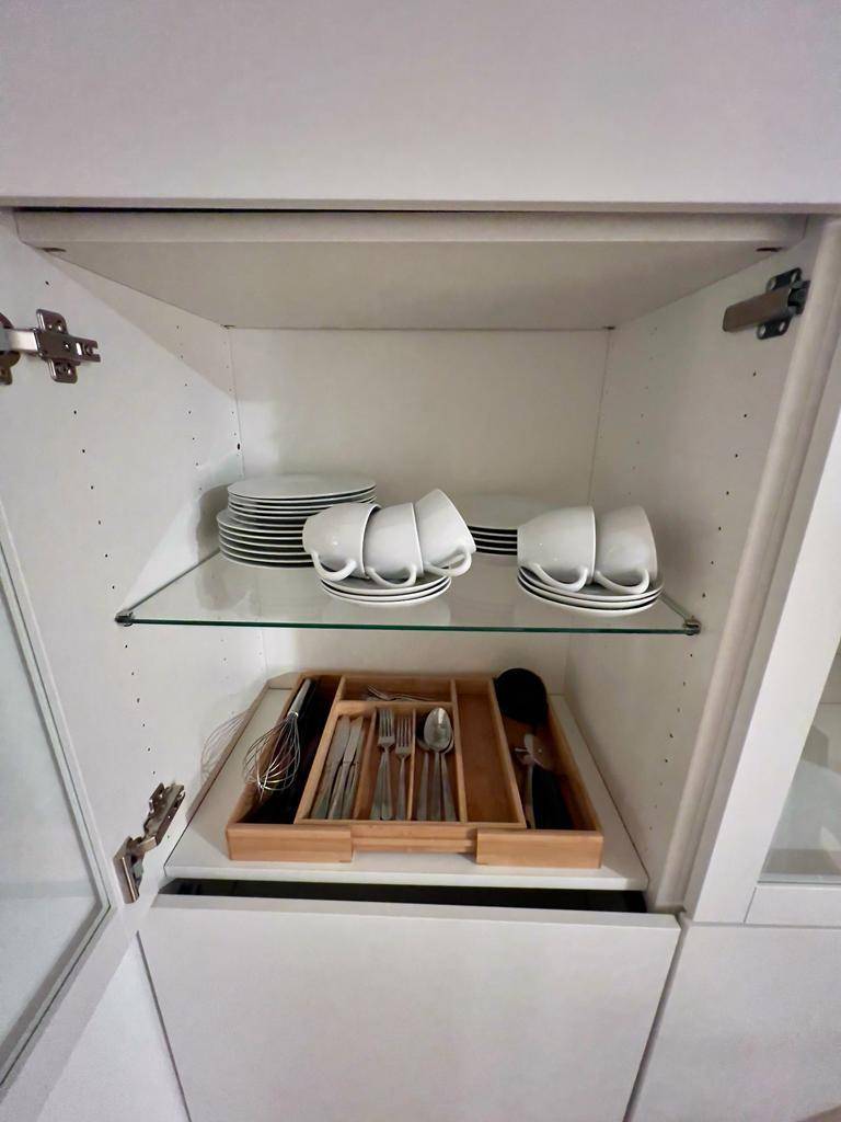 Offener Küchenschrank mit Geschirr, Tassen und Besteck in einer organisierten Schublade.