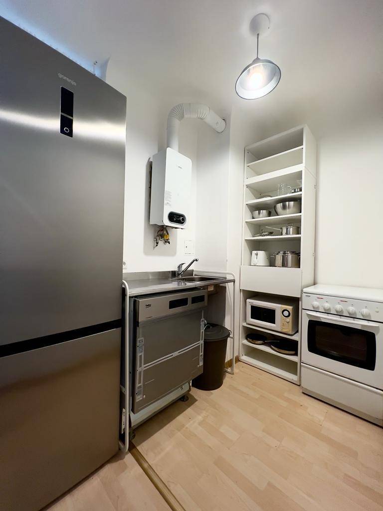 Kleine, funktionale Küchenzeile mit Kühlschrank, Herd, Mikrowelle und offenem Regal.