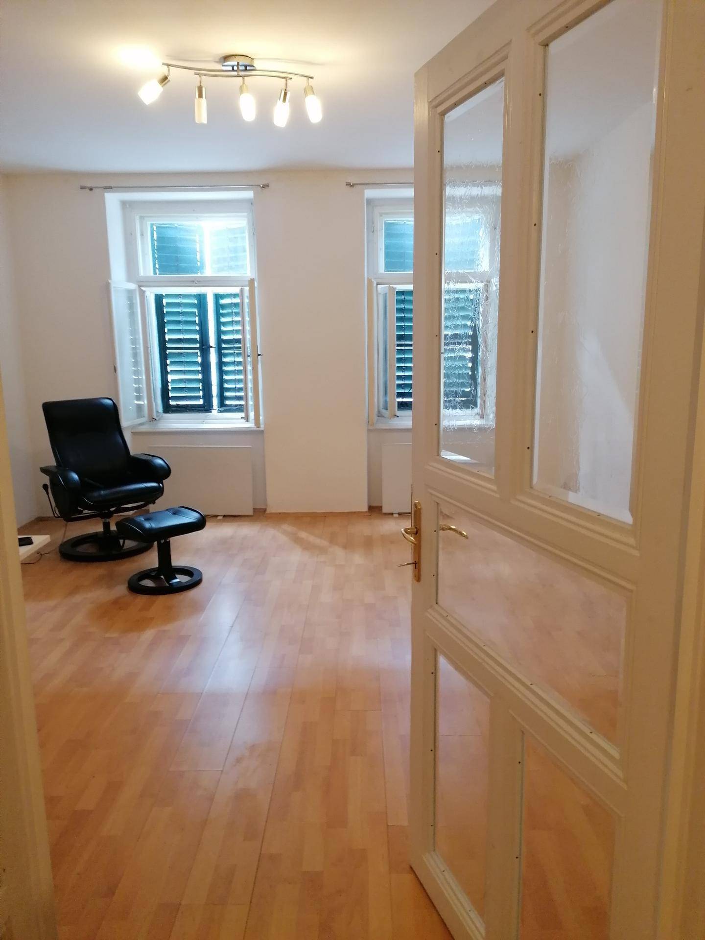Geräumiges Wohnzimmer mit Holzboden, zwei Fenstern und einer modernen Deckenleuchte.