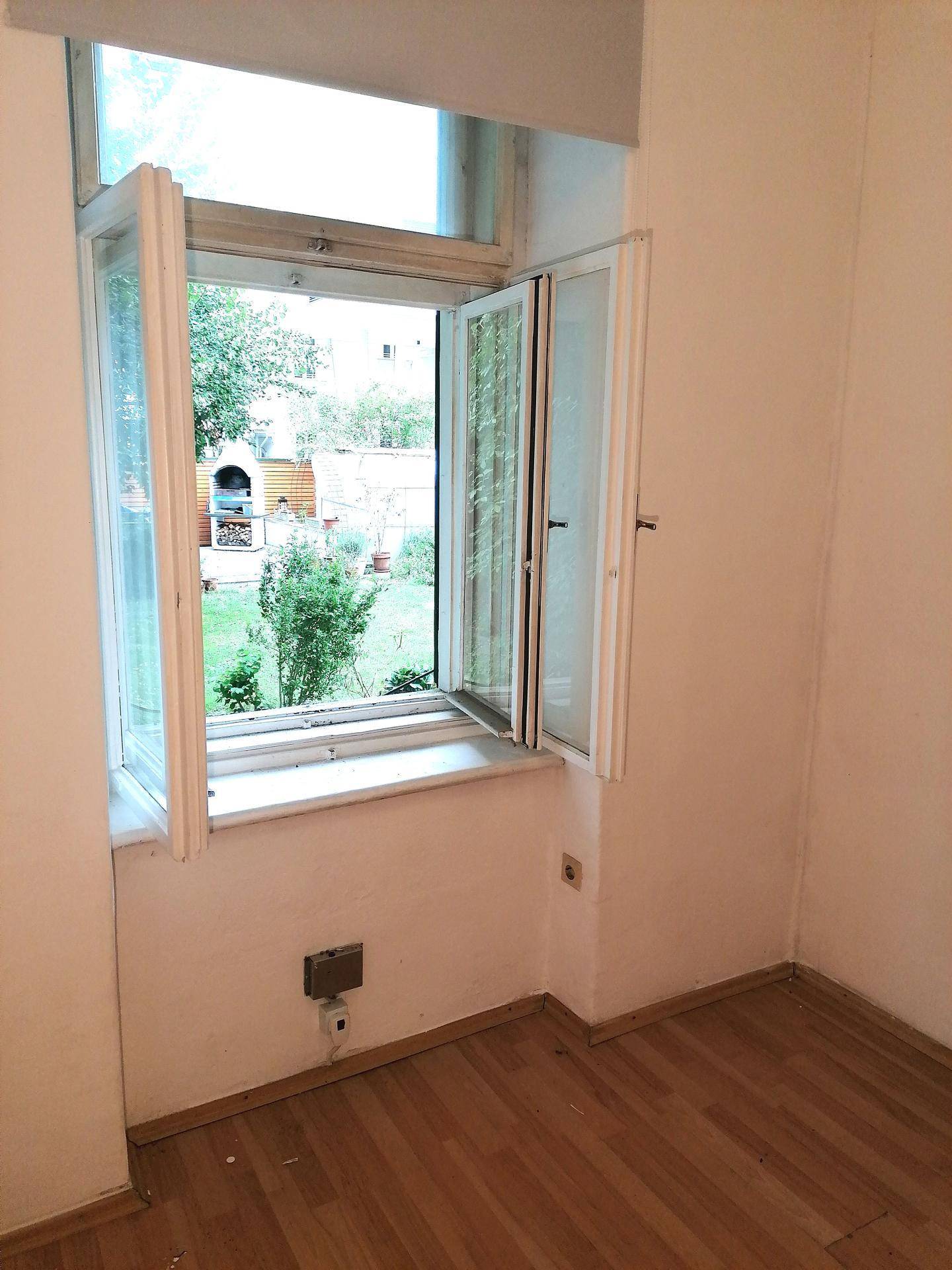 Helles Zimmer mit Holzboden und direktem Blick auf den Garten mit Grillplatz.