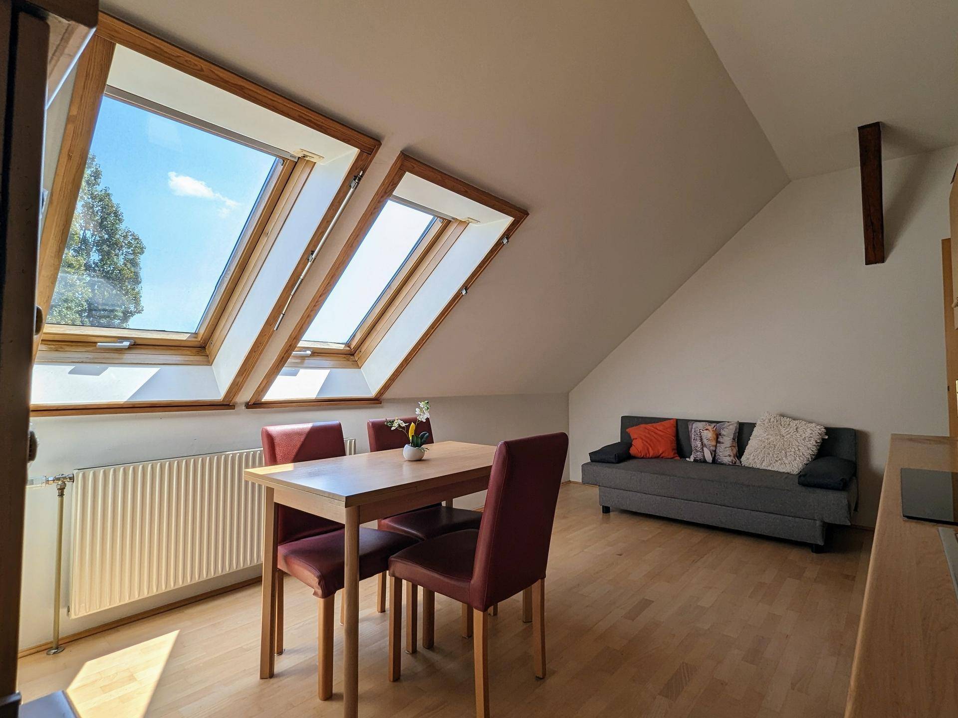 Gemütlicher Wohn- und Essbereich mit Holztisch, Sofa und großen Dachfenstern für viel Licht.