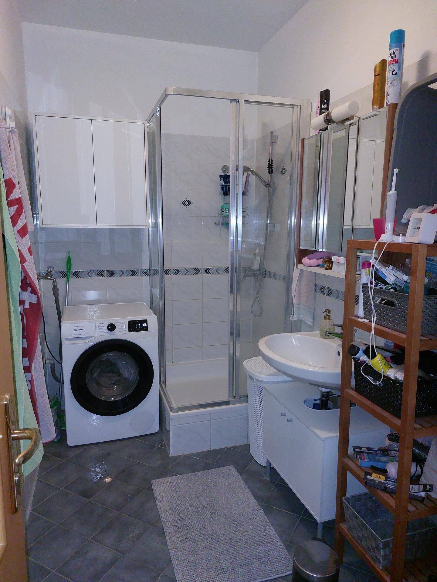Funktionales Badezimmer mit Duschkabine, Waschbecken und integrierter Waschmaschine.