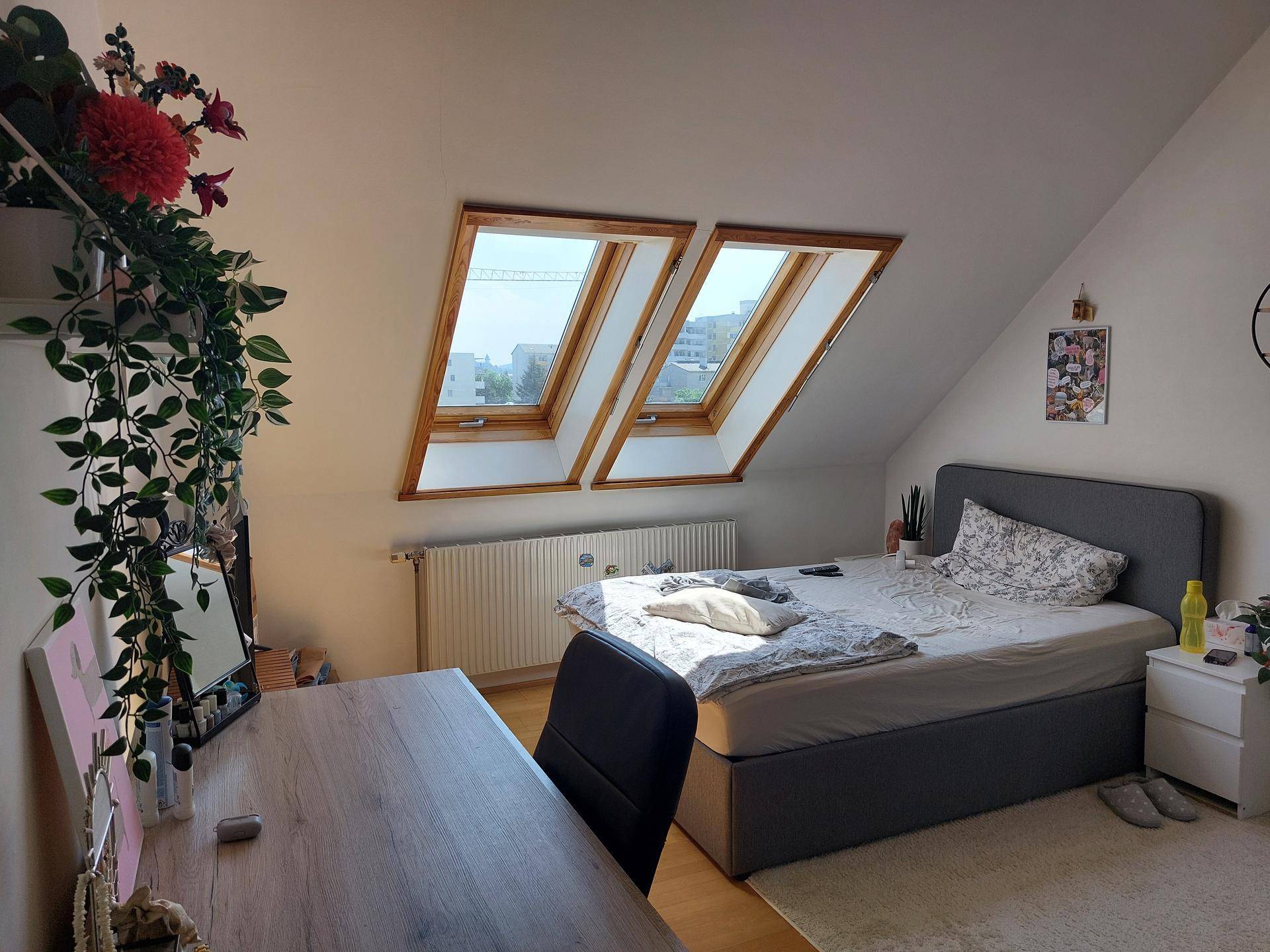 Schlafzimmer mit Bett, Schreibtisch und zwei großen Dachfenstern, die viel Tageslicht hereinlassen.