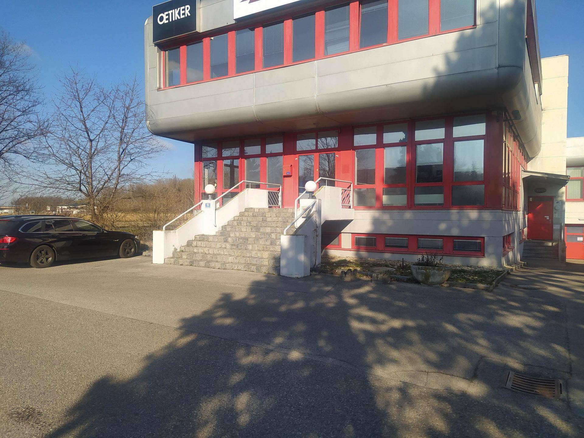 Nahaufnahme des Eingangs eines Geschäftsgebäudes mit breiter Treppe und roten Fensterrahmen bei sonnigem Wetter.